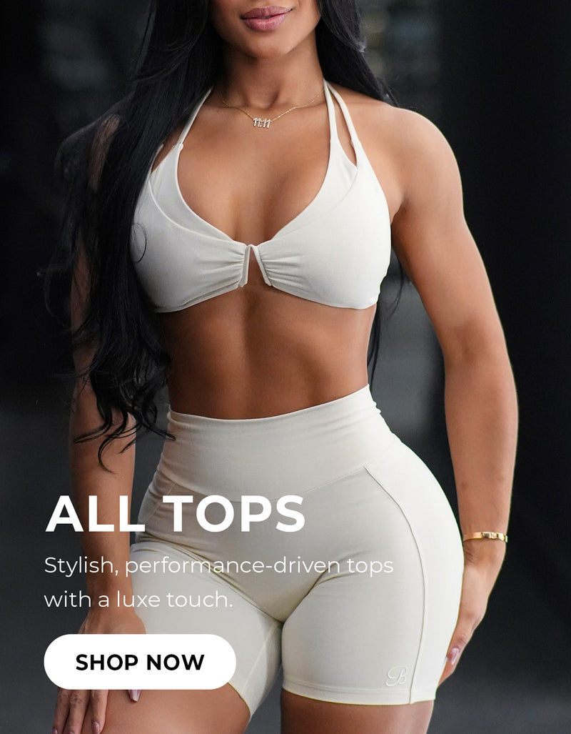 Model wearing a white sports bra and matching shorts. Promotional text reads: "ALL TOPS Stylish, performance driven tops with a luxe touch."